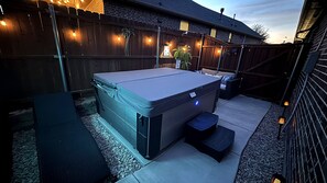 Een hottub in een openlucht setting, met een houten omheining en lichtjes.