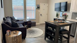 A modern living room with a dark brown sofa, a round coffee table, and a kitchen area with a flat-screen TV.