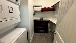 Ein Waschraum mit einer weißen Waschmaschine und einem Trockner, einem schwarzen Schrank und einem Regal mit einem roten Handtuch.