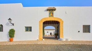 A white building with a large archway entrance, a small potted plant, and a tiled roof visible in the background.