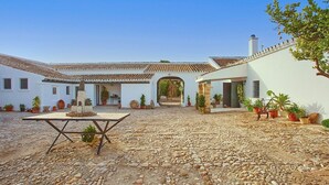 A courtyard with a table and chairs, surrounded by potted plants and a white building with a tiled roof.