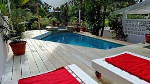 Relax by the serene pool surrounded by lush greenery and a shaded deck.