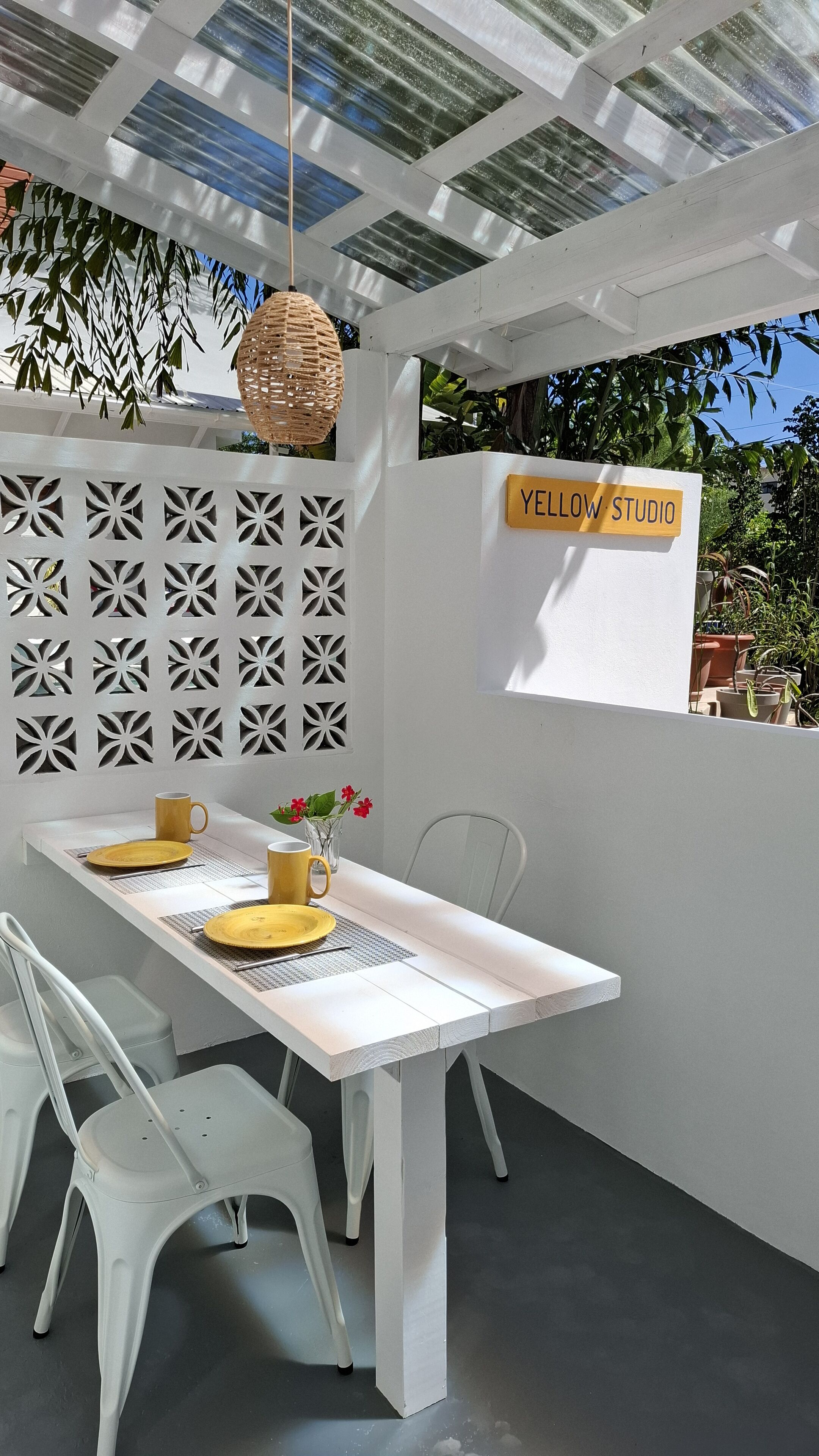 Un coin repas avec une table blanche, des assiettes jaunes et une tasse jaune. On peut y voir une enseigne sur laquelle est écrit « YELLOW W. STUDIO ».