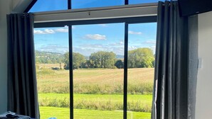 A bedroom with a large window, a bed, and a flat-screen TV. - Stunning modern home set in beautiful grounds. (Corston)