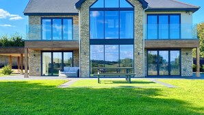 A modern two-story house with large windows, a stone facade, and a well-maintained lawn. - Stunning modern home set in beautiful grounds. (Corston)