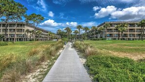 A pathway leading to a hotel with multiple floors and balconies, surrounded by greenery and palm trees. - 3rd Floor 100% Remodeled Condo- Ocean Views (Hilton Head Island)