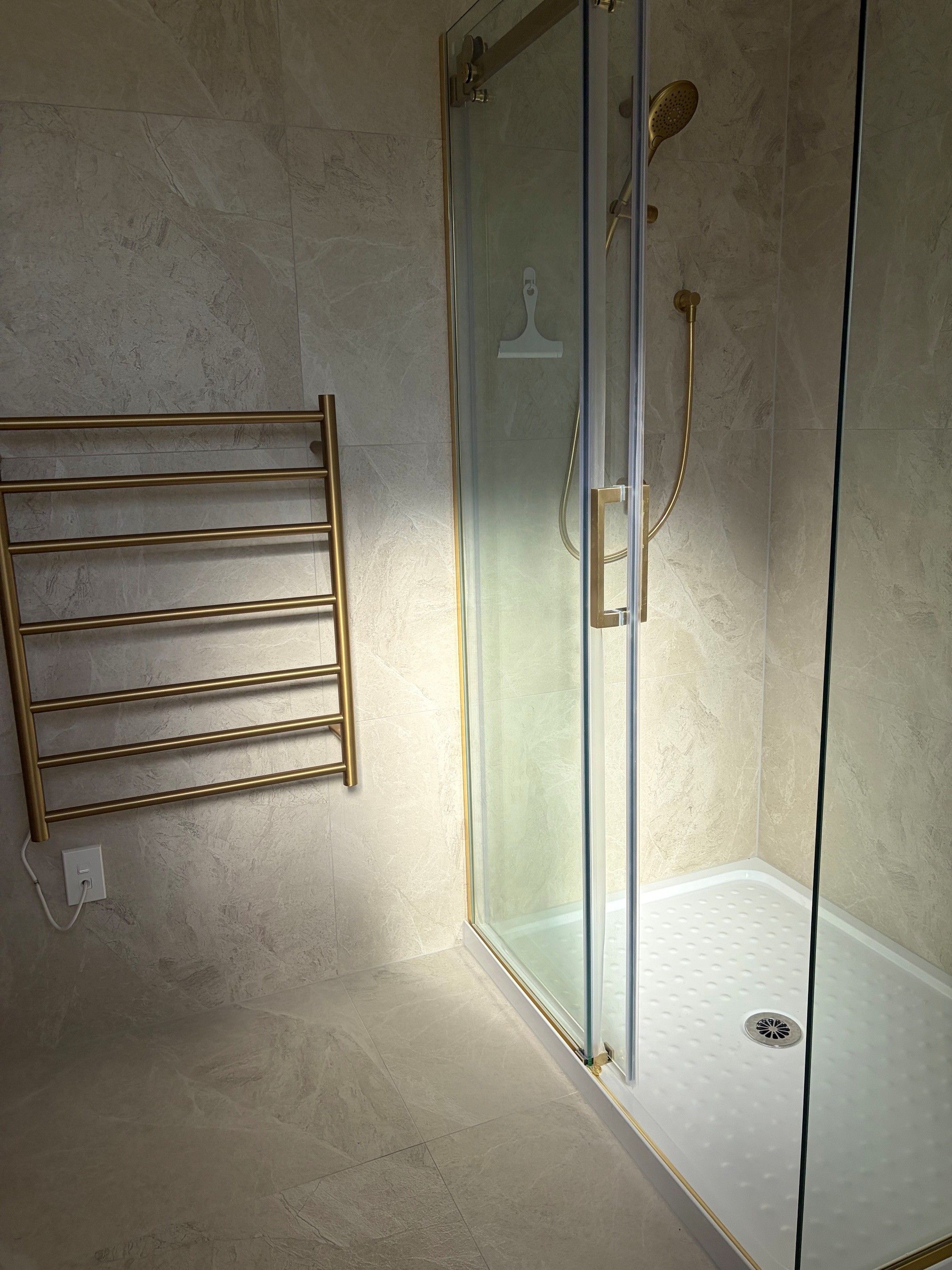 A glass-enclosed shower with a handheld showerhead and a wall-mounted towel rack.
