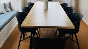 Spiseområde med et træbord, sorte stole, en hvid kande og en vævet pendel.