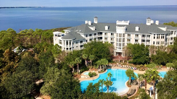 A large resort with a pool, surrounded by trees and overlooking a body of water.