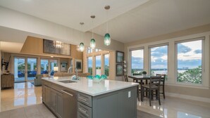 A spacious kitchen with a large island, modern pendant lights, and large windows offering a view of the city.