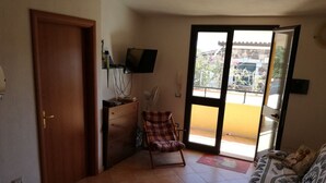 A room with a wooden door, a desk with a computer, a chair, a sofa with patterned cushions, and a sliding glass door leading to an outdoor area. - Vacation just 200m from the sea (Iscra E Voes)