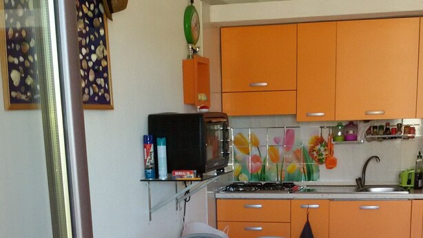 A compact kitchen with orange cabinets, a dining table with chairs, and a small refrigerator. - Vacation just 200m from the sea (Iscra E Voes)