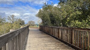 A wooden boardwalk with a metal railing, surrounded by trees and shrubs. - Coastal Vibes • Cal King Bed • Trails (Folsom)