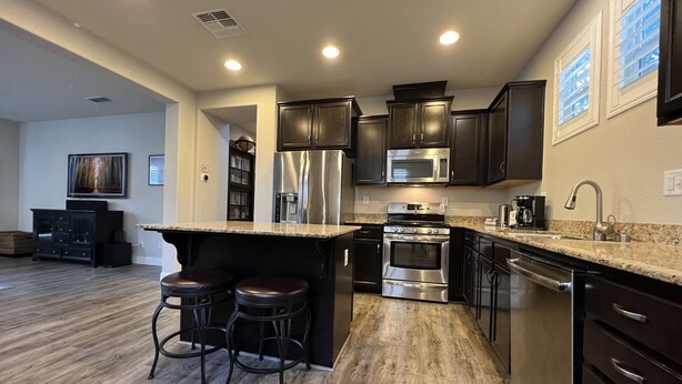 A modern kitchen with dark cabinetry, stainless steel appliances, and a granite countertop. - Coastal Vibes • Cal King Bed • Trails (Folsom)
