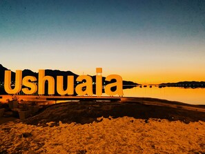 Une grande enseigne lumineuse, formant le mot « Ushuai'a », se détache sur le fond d’un coucher de soleil.