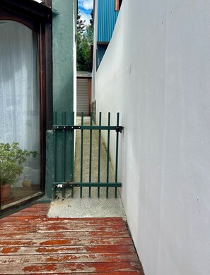 Un étroit sentier mène à un bâtiment doté d’une porte en métal verte, d’une plante en pot et d’un mur blanc.