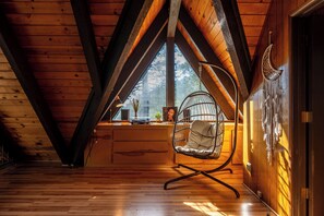 Ein Holzkaminzimmer mit schrägverdeckter Decke, einem Schaukelstuhl und einem großen Fenster.