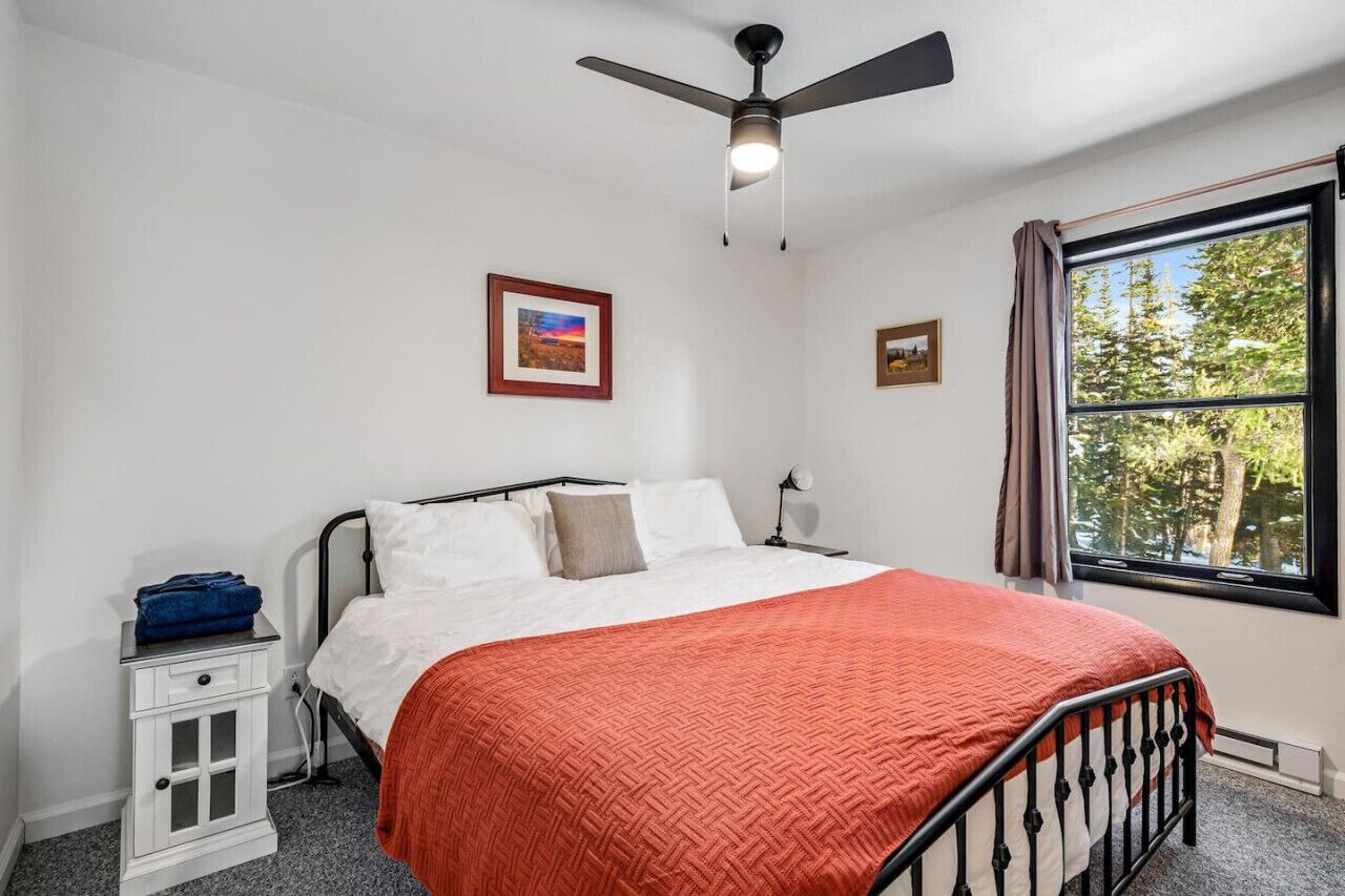 Una camera da letto con un letto, un comodino, una ventola a soffitto e una finestra vista alberi.
