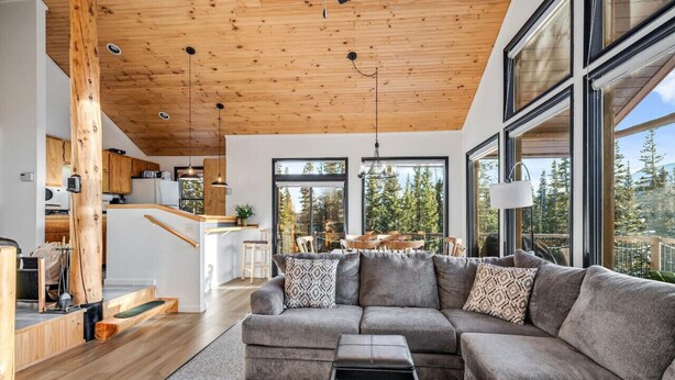 A modern living room with a large sectional sofa, a coffee table, and a view of a forest through large windows. - Secluded 3bed/Hot tub/Views (Fairplay)