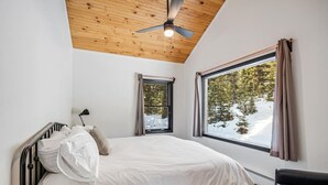 A bedroom with a bed, a ceiling fan, a window with curtains, and a view of trees and snow outside. - Secluded 3bed/Hot tub/Views (Fairplay)