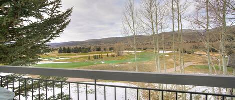 A view from a balcony overlooking a golf course with a river and mountains in the background.
