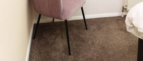 A room with a pink chair, a white radiator, and a wall with a framed sign that says "Be you".