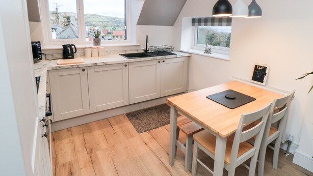 Een moderne keuken met witte kasten, een houten eettafel en uitzicht op het platteland door grote ramen.