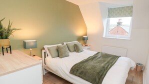 Een slaapkamer met een bed, nachtkastjes, een lamp, een plant en een raam met uitzicht.