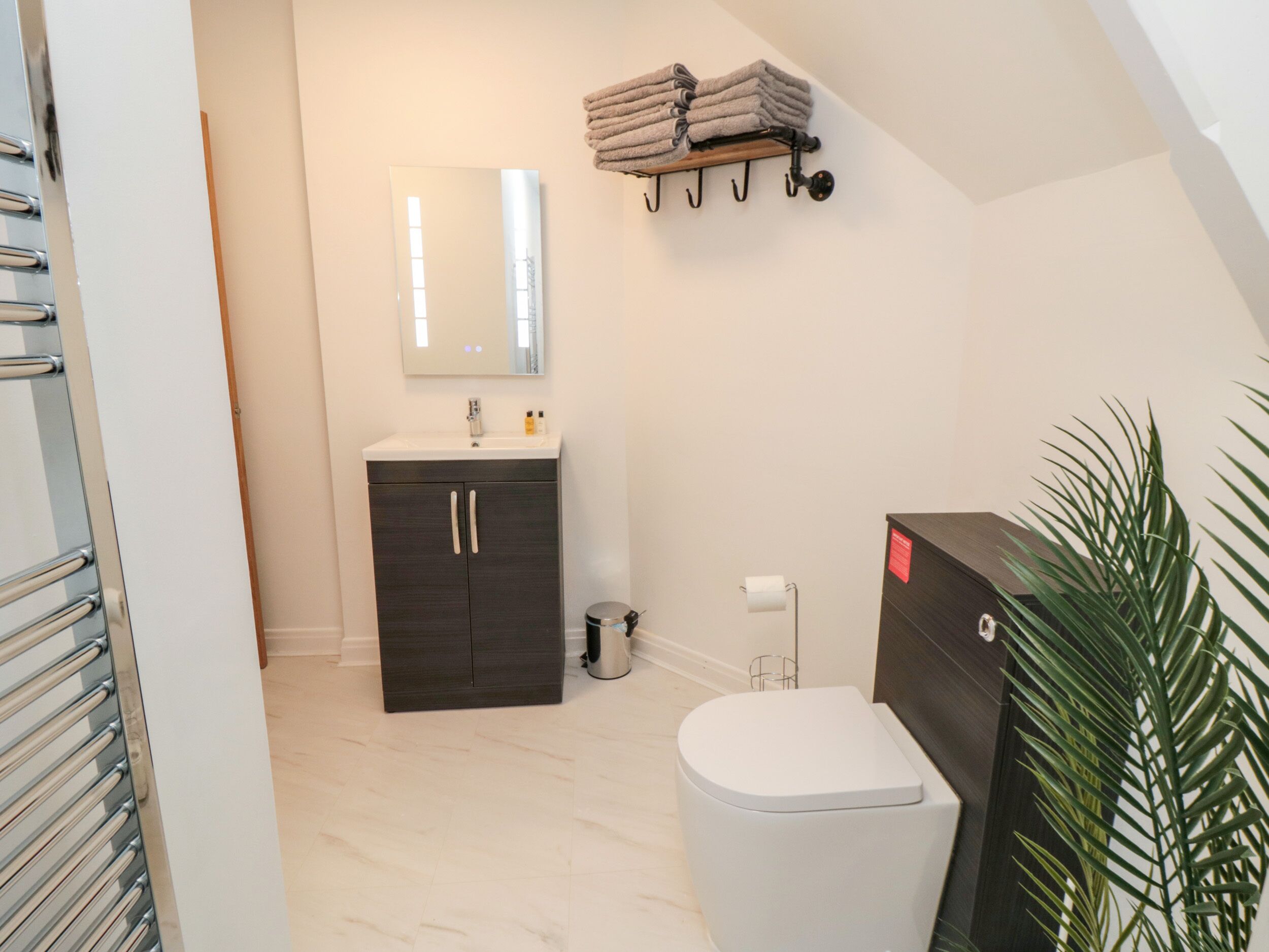 A modern bathroom with a white toilet, dark wooden cabinet, and a mirror above the sink.