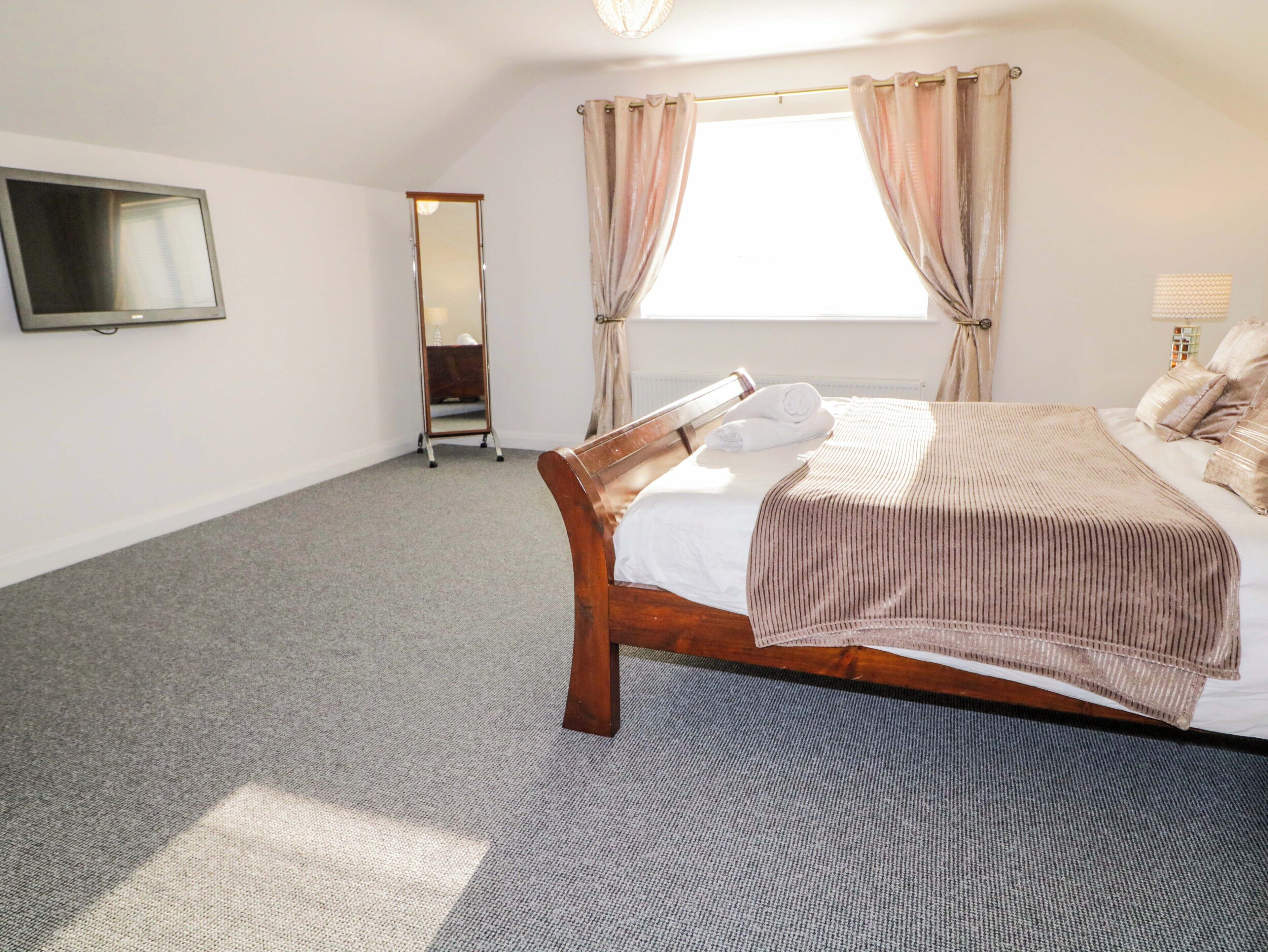 A bedroom with a bed, a mirror, and a window with curtains.