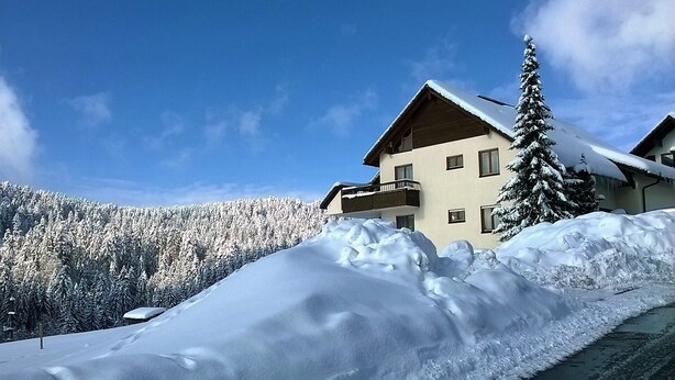 Ein schneebedeckter Berg mit einem Gebäude, das einen Balkon und einen schneebedeckten Baum zeigt.