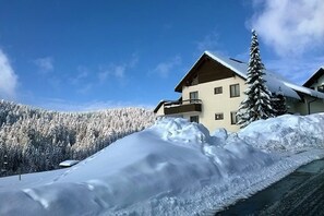 Una montaña nevada con un edificio que tiene un balcón y un árbol cubierto de nieve.