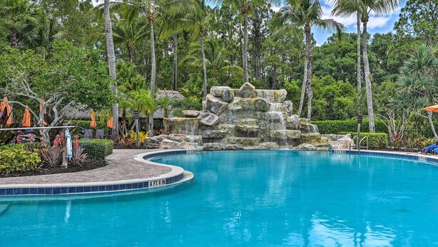 A pool with a rocky waterfall feature surrounded by palm trees and a brick walkway. - Ole at Lely Resort Condo w/ Pool Access! (Naples)
