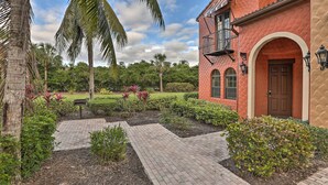 A red building with a balcony, surrounded by a garden with palm trees and shrubs. - Ole at Lely Resort Condo w/ Pool Access! (Naples)