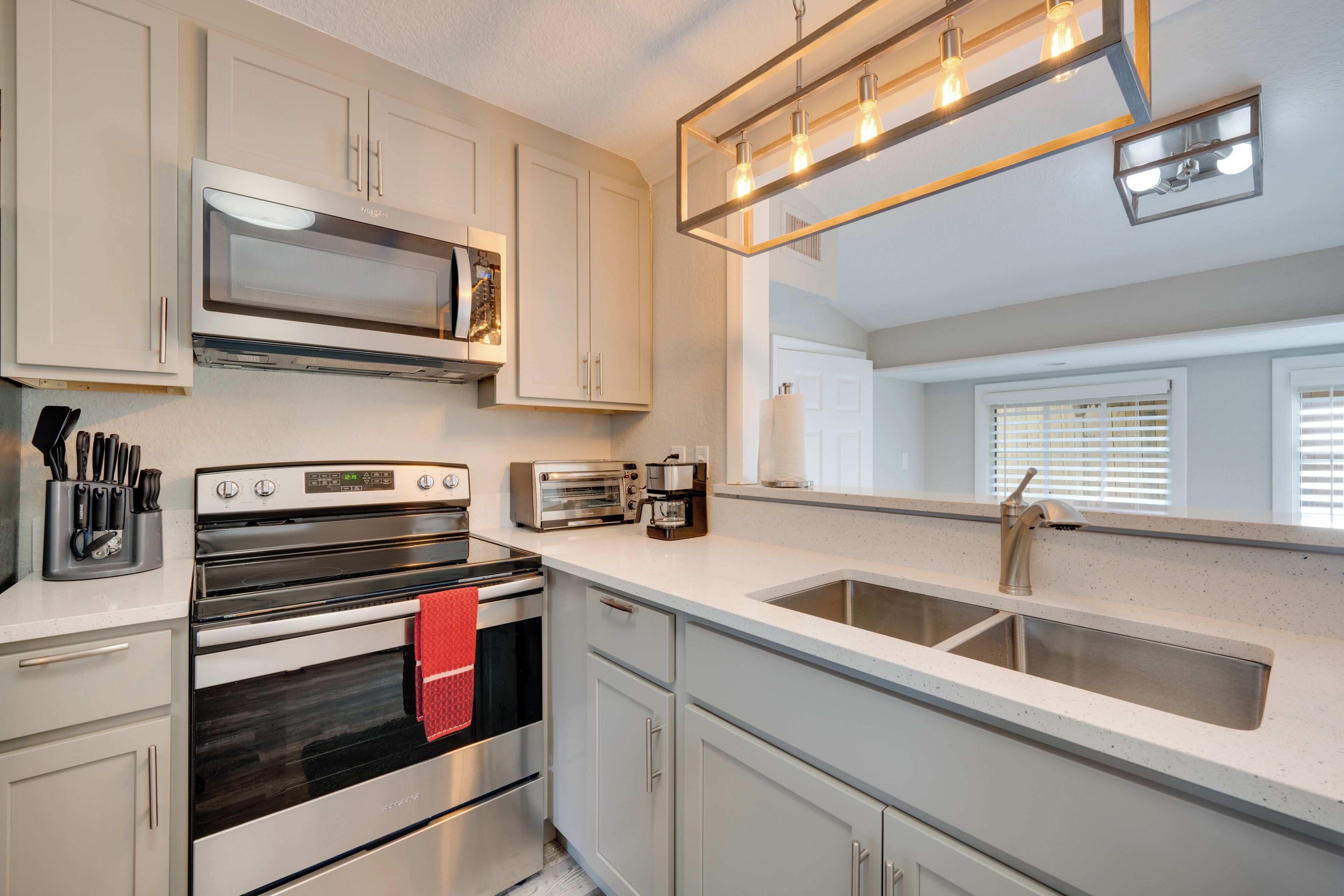 A modern kitchen with stainless steel appliances, a double sink, and a large window with blinds.