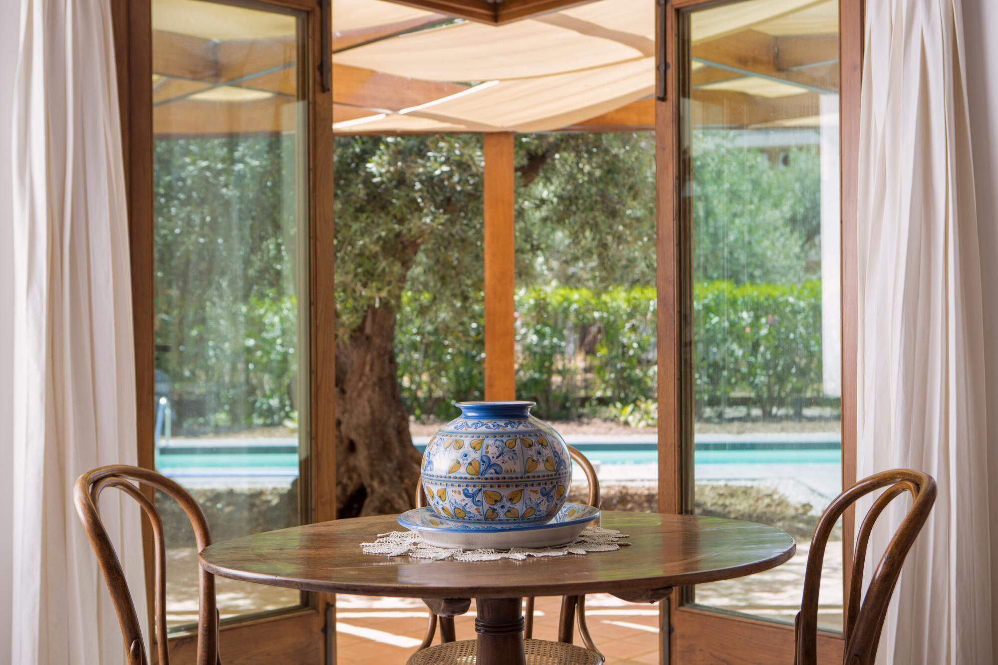 A round table with a decorative bowl and a lace doily, surrounded by wicker chairs, under a wooden umbrella.