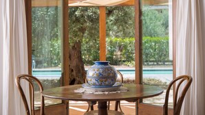 A round table with a decorative bowl and a lace doily, surrounded by wicker chairs, under a wooden umbrella.