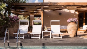 A poolside area with white lounge chairs, a large planter with pink flowers, and a pergola structure.