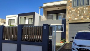 A modern two-story house with a gated entrance, a white car parked in front, and a garage door. - Beautiful House With Private Pool in Mauritius (Albion)