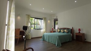 A bedroom with a bed, bedside tables, a chair, a standing fan, and a window with curtains. - Beautiful House With Private Pool in Mauritius (Albion)