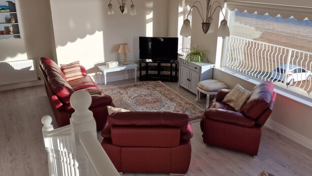 A living room with a red sofa set, a television, a small table with a lamp, and a view of the outside through a window. - Beach House (Duncannon)