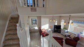 A spacious living area with a staircase, a red sofa, a television, and a view of the beach. - Beach House (Duncannon)