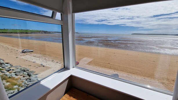 A room with a large window overlooking a beach. - Beach House (Duncannon)