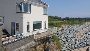A modern two-story house with a balcony overlooking a rocky beach. - Beach House (Duncannon)