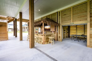 Un coin bar en bois avec des tabourets, un toit de chaume et une table de ping-pong.
