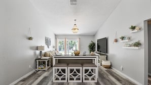 Uma sala de estar moderna com um console branco, assentos em banco e uma televisão.
