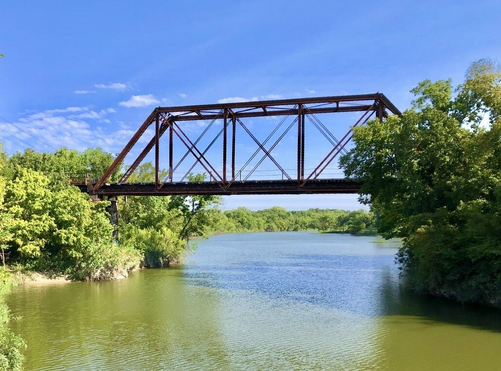 A metal bridge over a river with dense greenery on both sides.