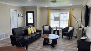 A living room with a black leather sofa, two armchairs, a coffee table, and a TV mounted on the wall. - Modern Home w/ Free WiFi near Seaworld! Small Dog Friendly (San Antonio)