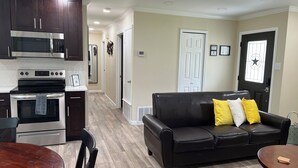 A modern kitchen with stainless steel appliances, a dining area with a wooden table, and a black leather sofa with yellow and white cushions. - Modern Home w/ Free WiFi near Seaworld! Small Dog Friendly (San Antonio)