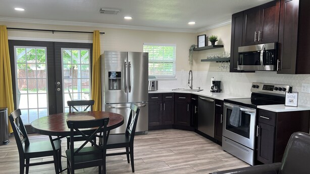 A modern kitchen with dark wood cabinets, stainless steel appliances, a dining table with chairs, and a view through a sliding glass door. - Modern Home w/ Free WiFi near Seaworld! Small Dog Friendly (San Antonio)